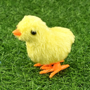Classic wind-up plush yellow chick toy jumping on green grass, nostalgic clockwork chicken