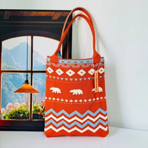 Close-up of orange knit tote bag featuring blue and white polar bear wave patterns