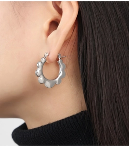 Close-up of woman wearing silver-tone wavy hoop earrings in a minimalist metal design