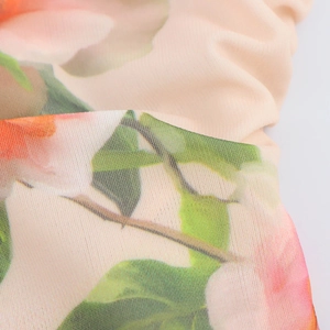 Dettaglio del tessuto a fiori con boccioli rosa e arancioni su materiale plissettato