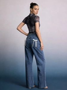 Détail d'un jean large avec un nœud en ruban blanc sur la poche arrière du pantalon
