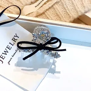 Détail d'une pince à cheveux à nœud noir avec perles argentées sur une carte à bijoux blanche