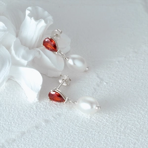 Macro shot of S925 sterling silver pearl earrings with orange zircon on floral background