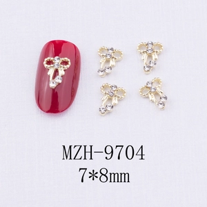 Détail de bijoux d'ongles nœuds dorés 7x8mm avec strass présentés sur un ongle rouge