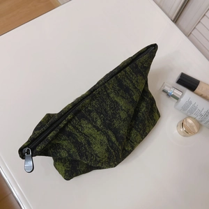 Vintage green and black jacquard makeup bag with metal zipper on a white counter