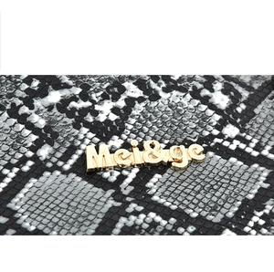 Macro view of snakeskin textured leather and golden metallic Mei&ge brand logo detail