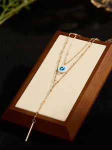 Double-layered gold Evil Eye Y-shaped tassel necklace displayed on a wooden stand