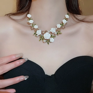 Close-up of floral necklace with white roses, pearls and green leaves on a gold chain