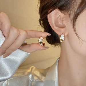Detail view of French-style gold textured earrings with green teardrop zircon and pearl