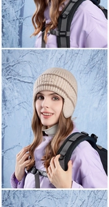 Dettaglio del cappello in maglia beige con paraorecchie e logo in una foresta innevata