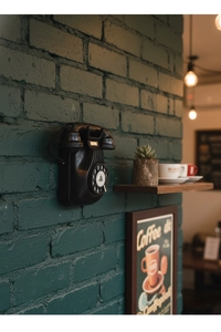 Detail of vintage wall-mounted rotary telephone on a green brick wall with warm lighting