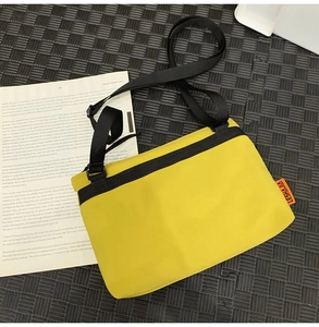 Overhead view of yellow nylon crossbody messenger bag with black adjustable strap and tag