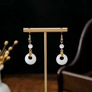 Detail of Chinese style tassel earrings with white jade rings on a gold display stand
