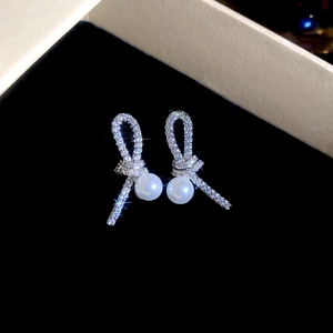 Detailed view of silver knot earrings with pavé crystals and elegant white pearls