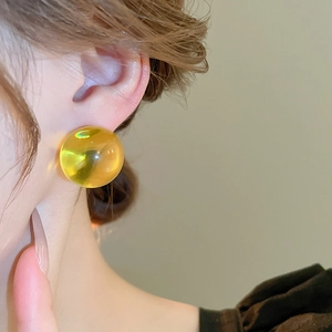 Gros plan d'une boucle d'oreille boule en résine ambre sur un modèle au style épuré