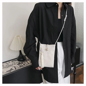 White satin phone bag featuring a pearl clasp and tassel accessory shown on a model