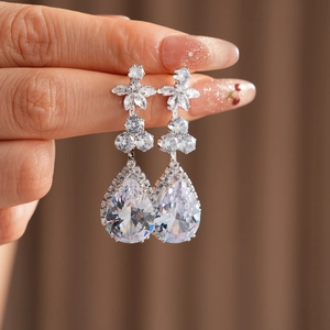 Detailed close-up of silver-plated flower and teardrop zircon earrings held by hand