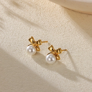 Detail view of gold bow pearl earrings featuring polished metal and round white pearls