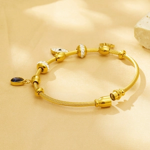 Detail of gold twisted cable bracelet with evil eye charm and blue stone pendant