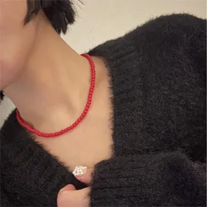 Primo piano di una collana minimalista di perle rosse indossata da una modella in maglione