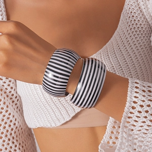 Dettaglio di due grossi bracciali in acrilico con strisce bianche e nere su una modella