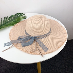Detail of a straw sun hat featuring a blue lace ribbon and fringed wide brim edges