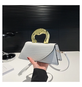 Detail of white crocodile-embossed handbag with unique irregular gold metal handle and strap