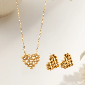 Détail macro du collier et des boucles d'oreilles cœur dorés avec texture maille sur fond beige