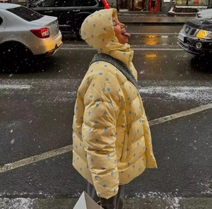 Close-up of a yellow floral hooded puffer jacket worn by a model in a snowy street