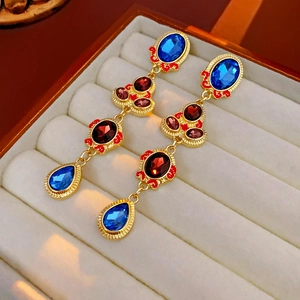 Detail of vintage gold earrings with blue and red oval gemstones in a beige velvet box