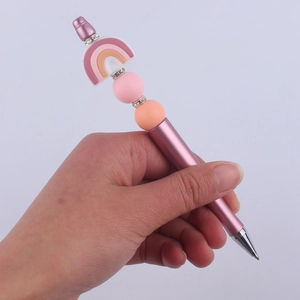 DIY beaded pen with rainbow silicone charm and pink beads held in hand for scale