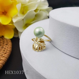 Detail view of gold monstera leaf ring featuring a green pearl on a white pedestal