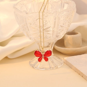 Elegant gold chain necklace with a red crystal butterfly pendant on a glass rim