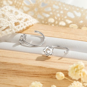 Minimalist silver C-shaped hoop earrings with star charms on a soft wooden background