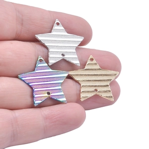 Three-color stainless steel star pendants with striped texture held in palm for scale