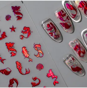 Detail showing holographic red mermaid and seashell nail stickers on artificial nails