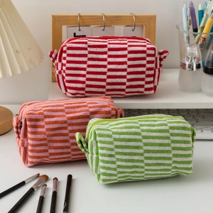 Three knit checkered cosmetic bags in red, pink, and green on an organized desk