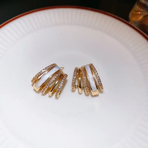 Detail view of gold C-shaped layered earrings with white mother-of-pearl and zircon