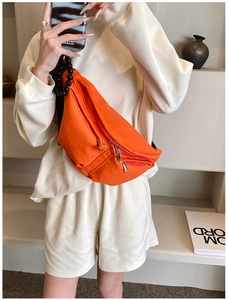 Detail of vibrant orange nylon chest bag with silver zippers and black bead handle strap