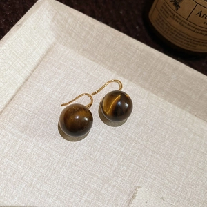 Macro detail of sphere tiger eye earrings with gold hooks on a beige textured tray
