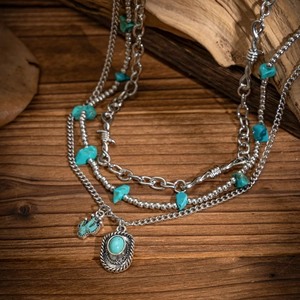 Detail of layered turquoise necklaces with silver cactus charms on a rustic wood background