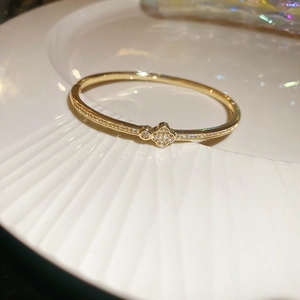 Macro shot of a gold clover charm bracelet with sparkling zircons on a white plate