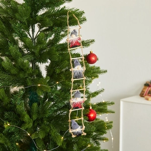 Detail of wooden ladder gnome ornaments hanging on a Christmas tree with festive lights