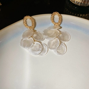 Detail of round shell tassel earrings with gold textured rings on a white plate
