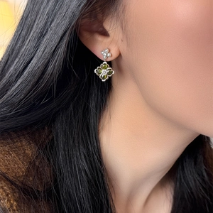 Close-up of four-leaf clover earrings with green gemstone and small white pearls on model
