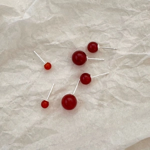 Macro shot of red agate stud earrings in various sizes on a textured white paper background