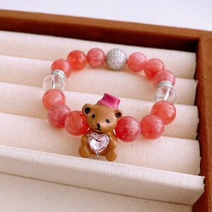 Détail d'un bracelet en perles avec un charm ours marron et un cœur en cristal rose