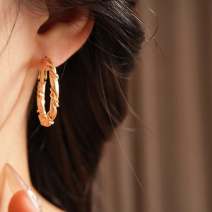 Close-up of a model wearing a golden twisted hoop earring with detailed braided texture