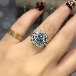 Macro shot of silver floral halo ring with brilliant round center stone on model's hand
