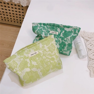 Close-up of green floral jacquard canvas makeup bags with simple wish labels on a white desk